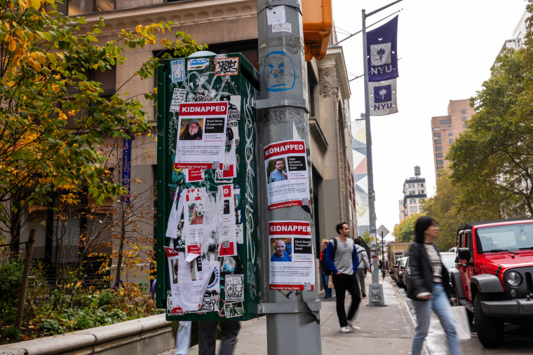 People walk by posters of some of those kidnapped by Hamas from Israel on a pole